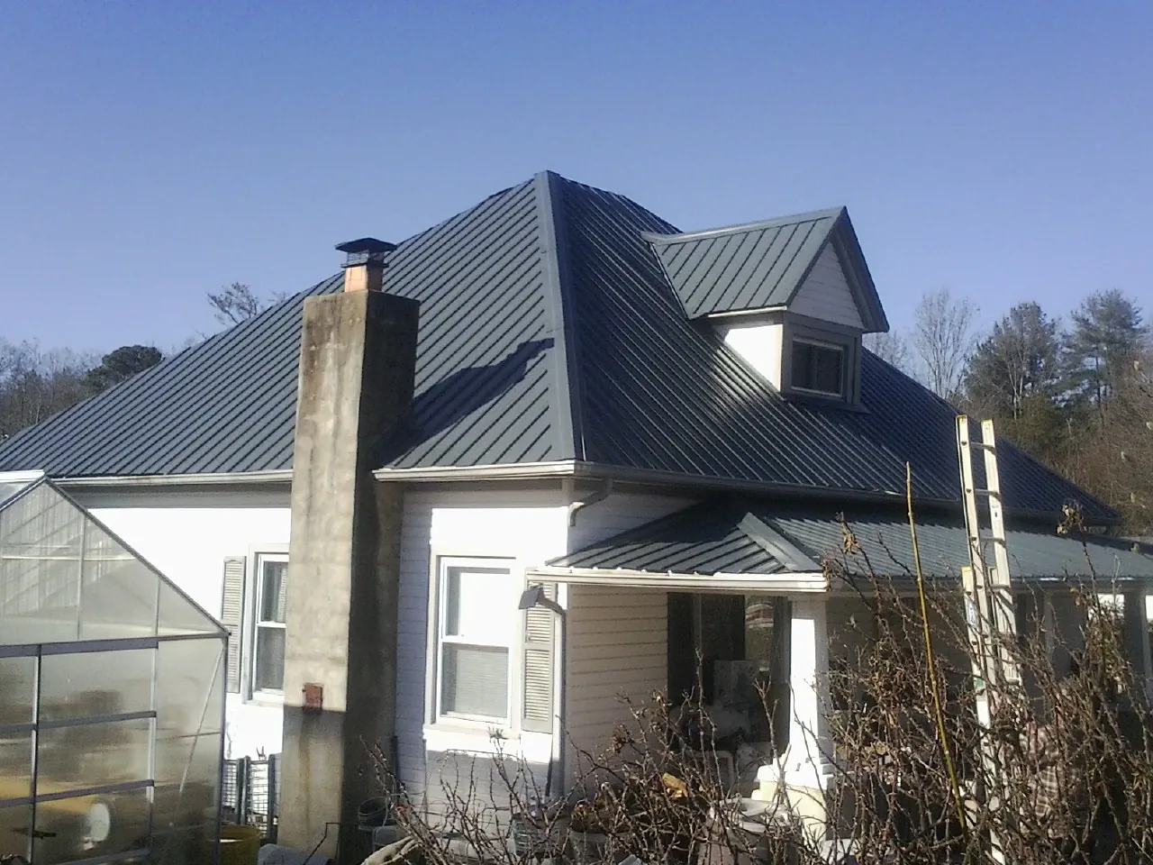 Dark blue standing seam metal roof on a white farmhouse with dormer — Slate & Tile Roof Repair by Roofing Brothers in Nichols