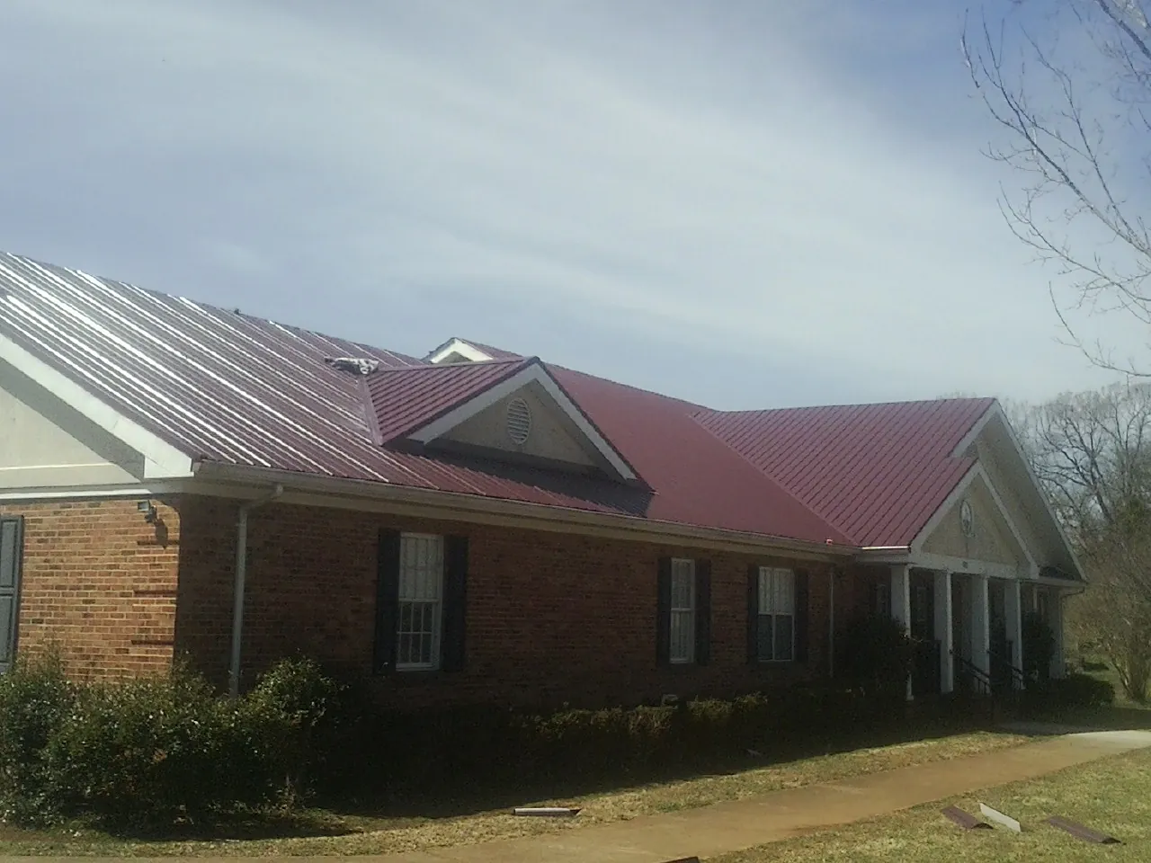 Red metal roof with gabled entries on a long brick building, from a Hail Damage Roof Repair job in Nichols