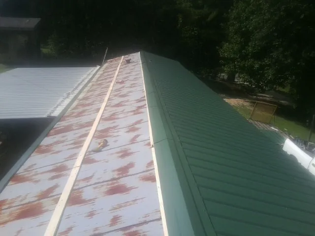 Old rusted panels beside newly installed green metal roofing — Wind Damage Roof Repair by Roofing Brothers in Nichols