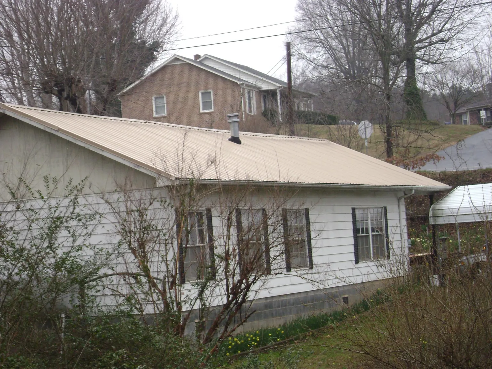 Tan metal roof on a white sided house set into a hillside — Commercial Roofing by Roofing Brothers in Nichols