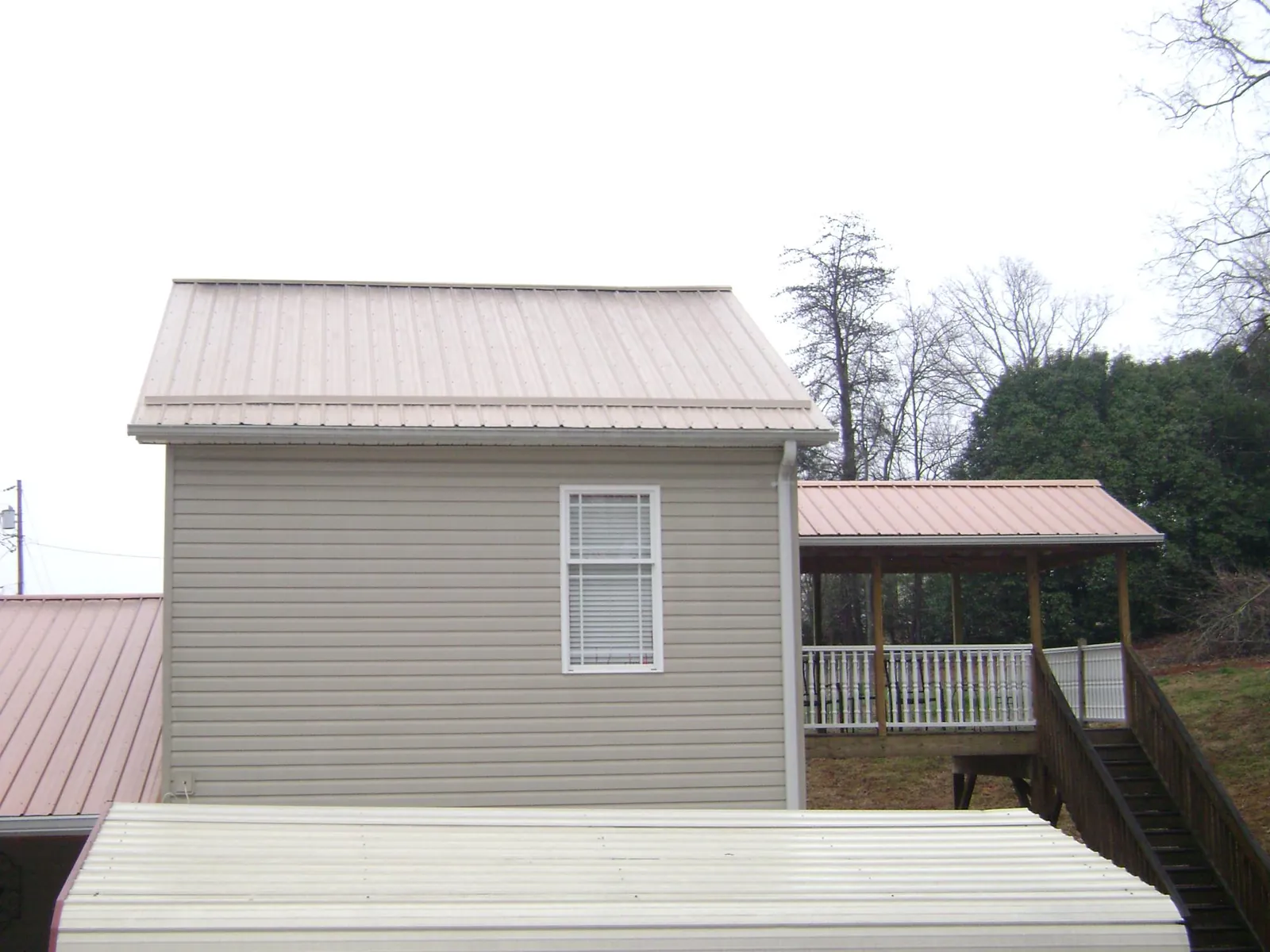 Tan metal roofs on a two story addition and attached porch, from a Roof Replacement job in Nichols